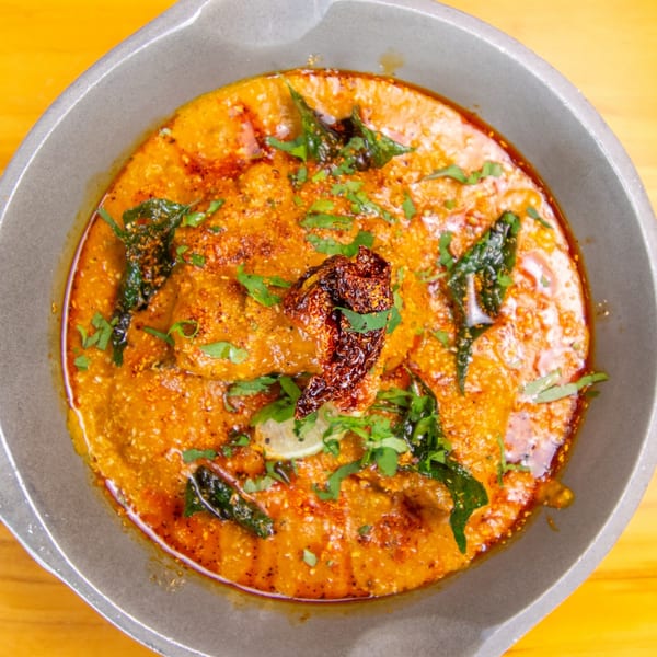 Close-up of a vibrant orange curry dish, garnished with fresh herbs, dried chili, and lime.
