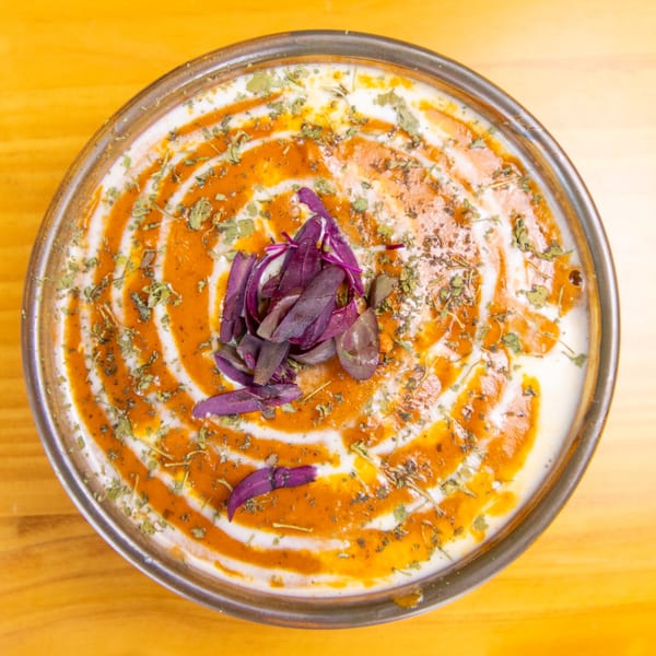 Overhead view of a dish with white sauce, orange swirls, dried herbs, and purple leaves.