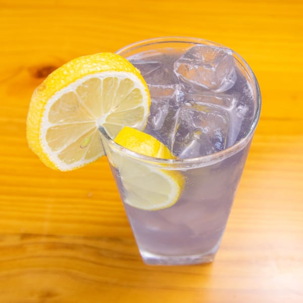 A refreshing drink with ice and lemon slices in a clear glass on a wooden table.