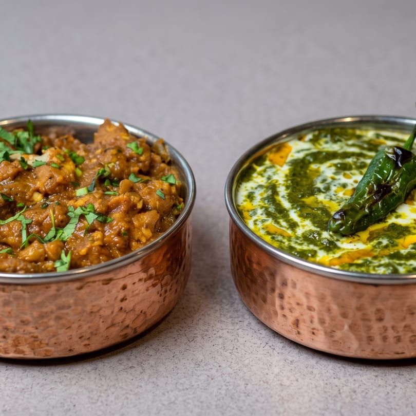 Two copper bowls filled with Indian dishes: a brown curry with cilantro and a green spinach dish with cream.