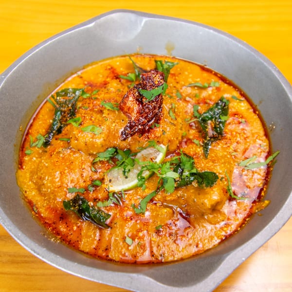 Close-up of a vibrant orange curry dish, garnished with herbs, lime, and a dried red chili.