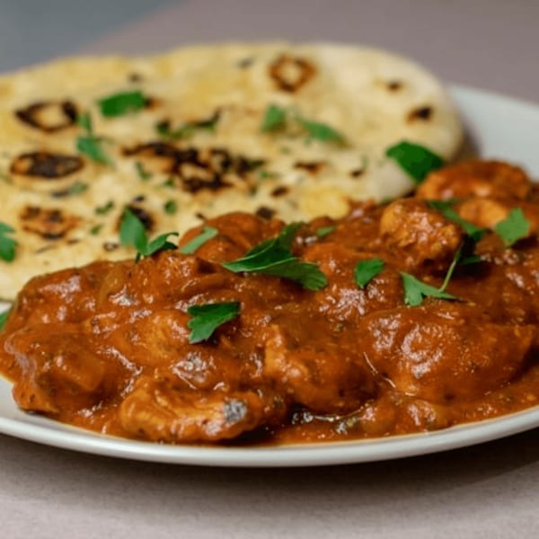 Chicken tikka masala with naan bread, garnished with fresh cilantro on a white plate.