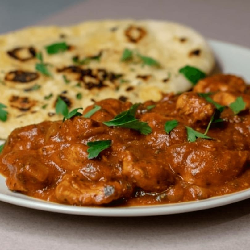 Chicken tikka masala with naan bread, garnished with fresh cilantro on a white plate.
