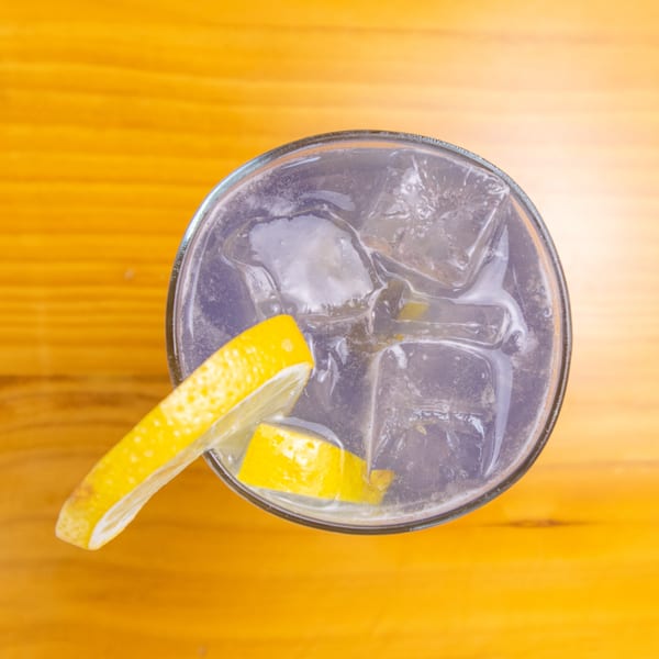 Overhead view of a clear drink with ice and lemon slices on a wooden table.