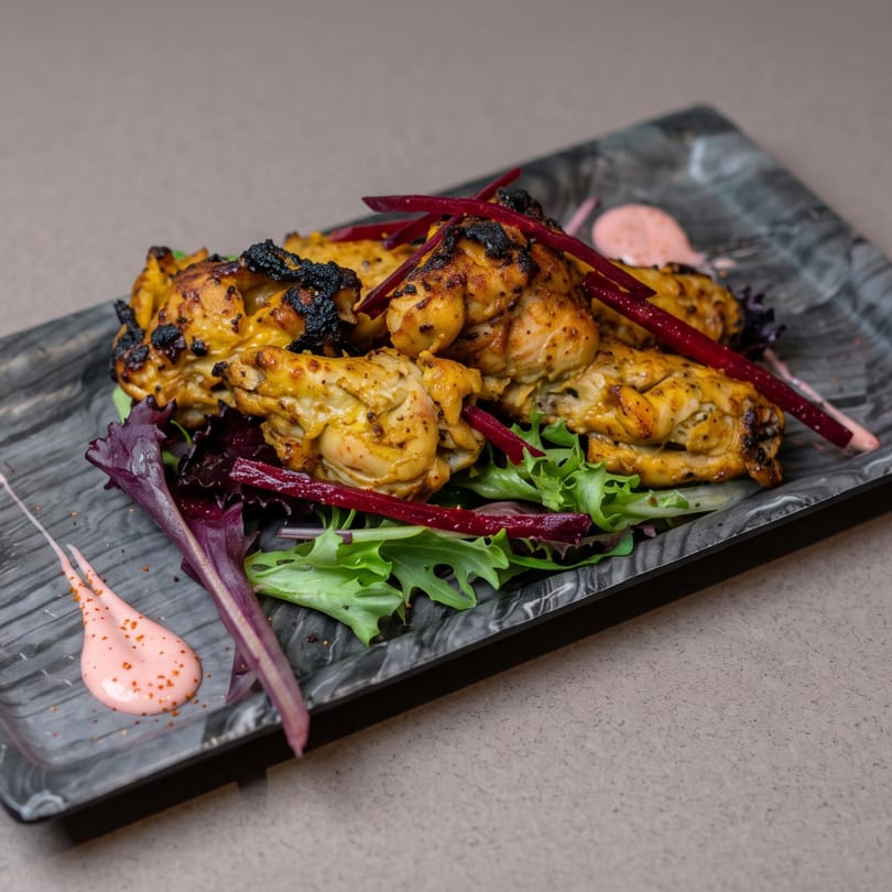 Grilled chicken pieces with charred edges on a bed of mixed greens, garnished with red beet strips and pink sauce.