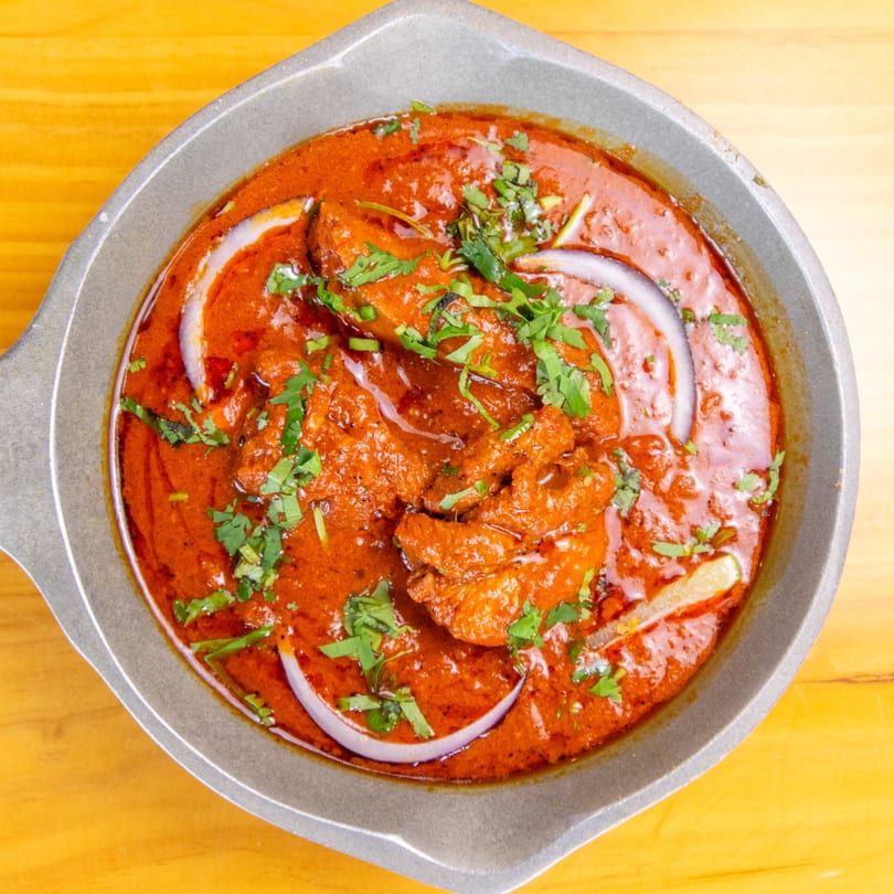 Close-up of a vibrant red curry dish, garnished with fresh cilantro, red onion, and lime.