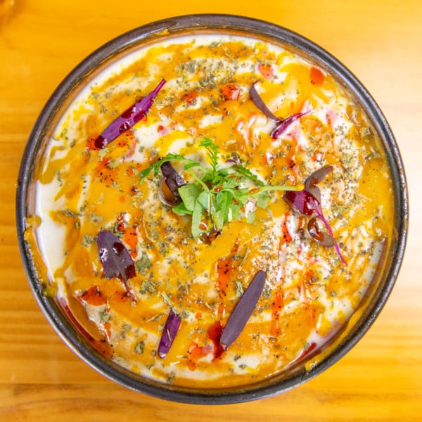 Overhead view of a creamy dish with orange sauce, red chili oil, dried herbs, and fresh greens.