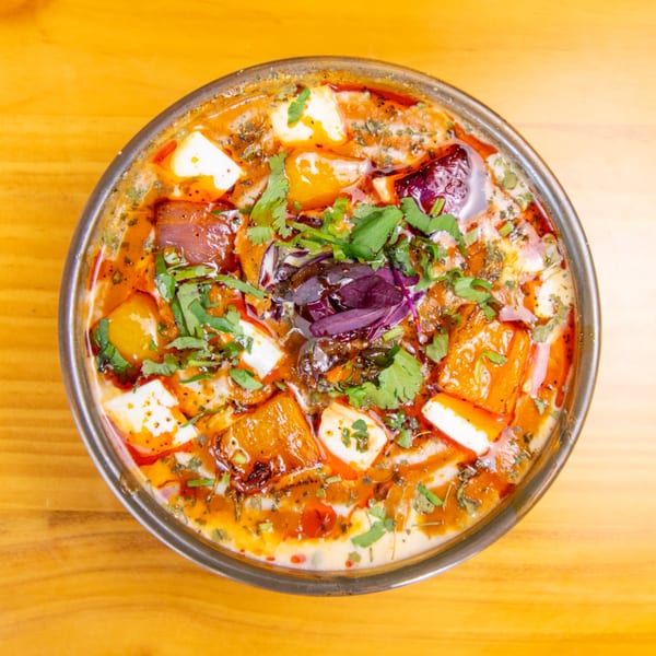 Overhead view of a vibrant Indian curry with paneer, vegetables, and fresh herbs in a metal bowl.