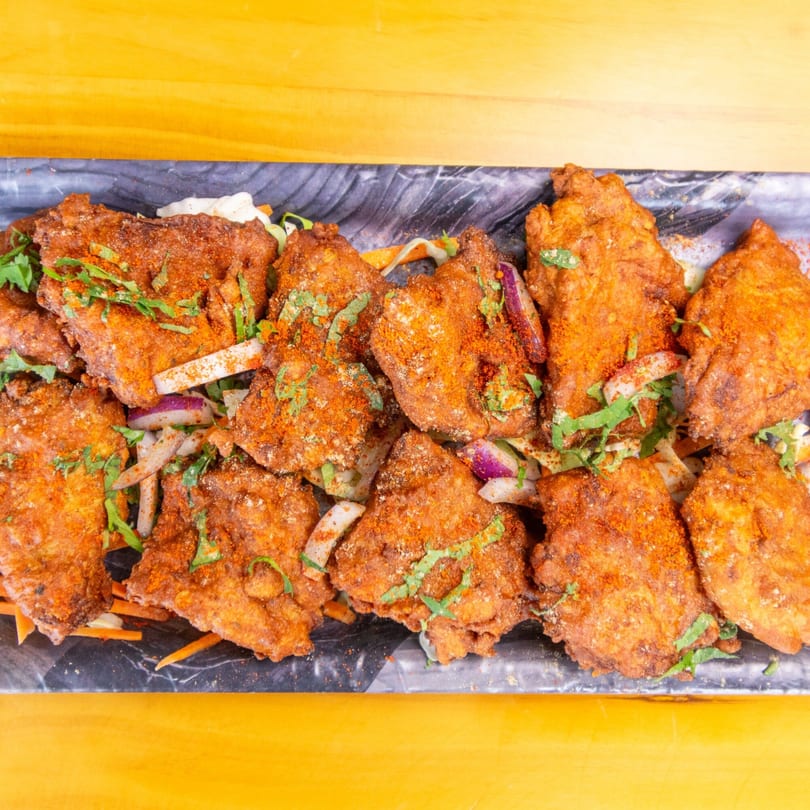 Crispy fried chicken pieces, seasoned with red spice and fresh cilantro, served on a dark platter.