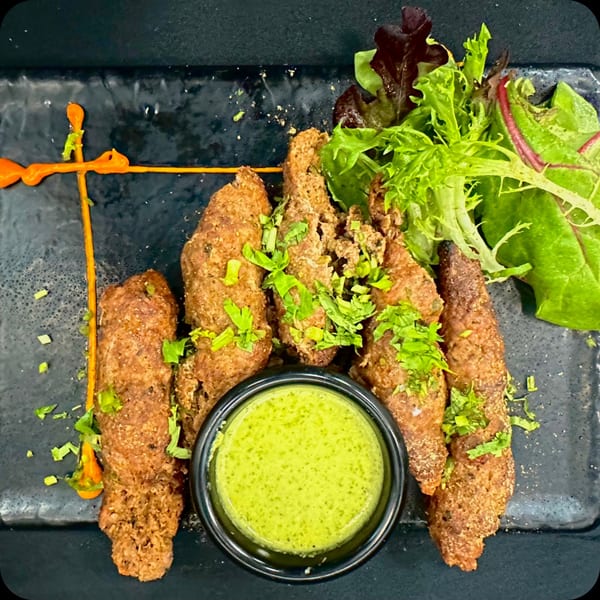 Five brown, crispy fried appetizers with green herbs, a side of green sauce, and a small salad.